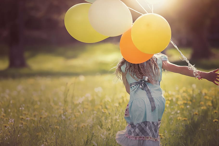 selectivo, fotografía de enfoque, niña, azul, vestido, tenencia, amarillo, globos, jugando, campo de hierba