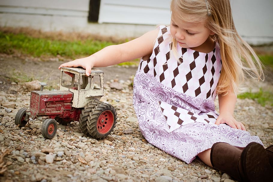 girl, white, purple, sleeveless dress, playing, red, toy car, daytime, country, farm