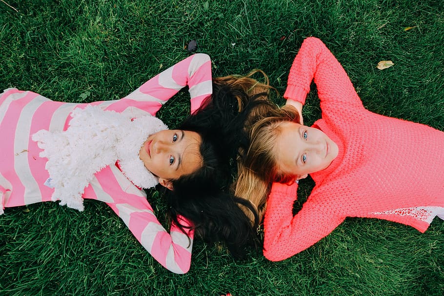 two, girls, wearing, pink, white, long-sleeved, shirts, lying, grass, daytime
