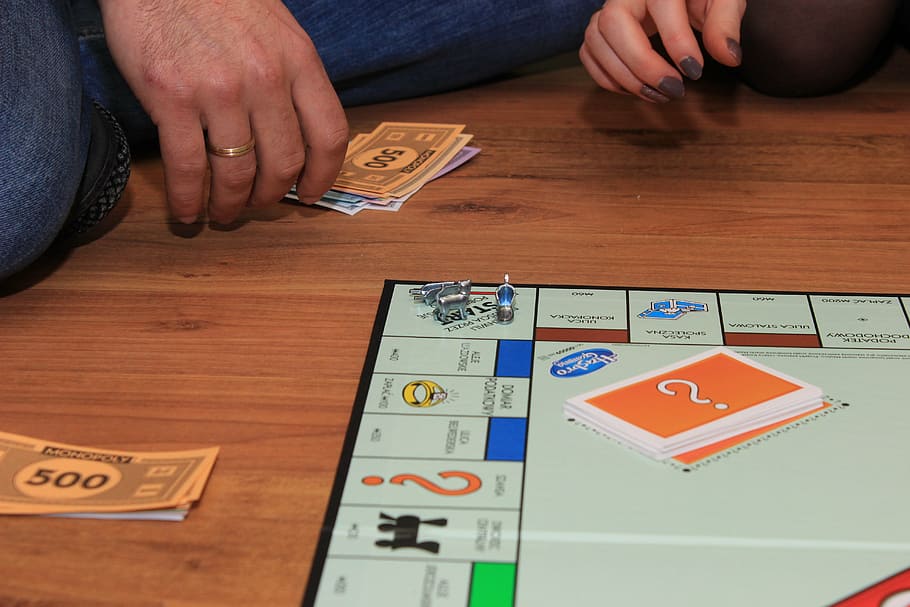 person playing gameboard, monopoly, game, board game, human hand, hand, human body part, indoors, table, currency