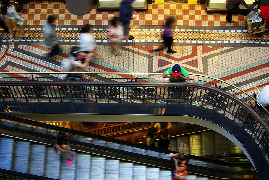 man, leaning, gray, metal hand rail, mall, busy, shopping, retail, shopper, escalator
