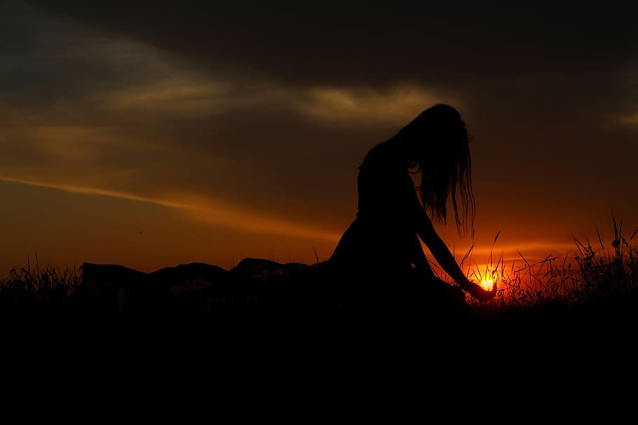 silhouette photography, woman, sitting, grass, grey, clouds, orange, skies sunset, sun, shadows