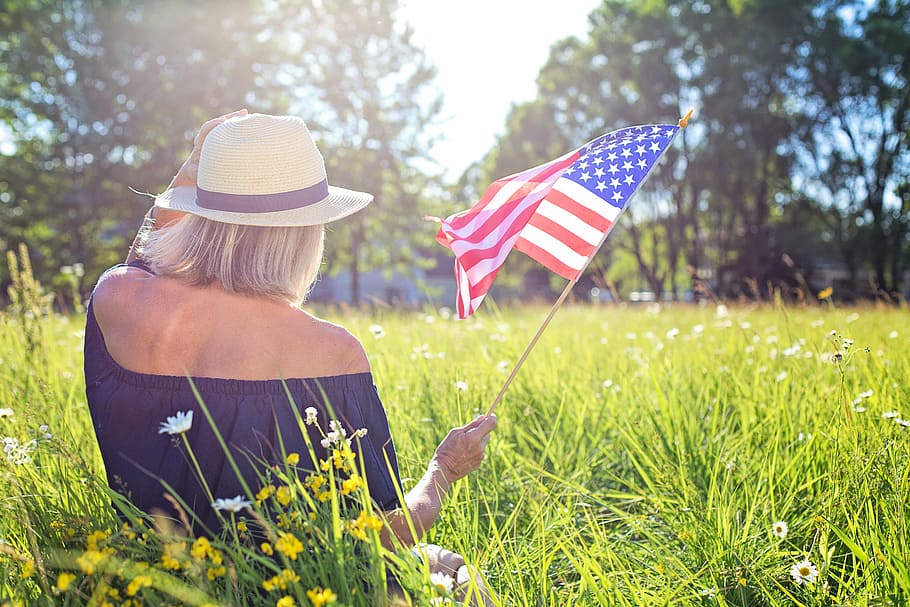 woman, holding, u.s.a flag, sitting, green, grass field, daytime, fourth of july, waving flag, american flag