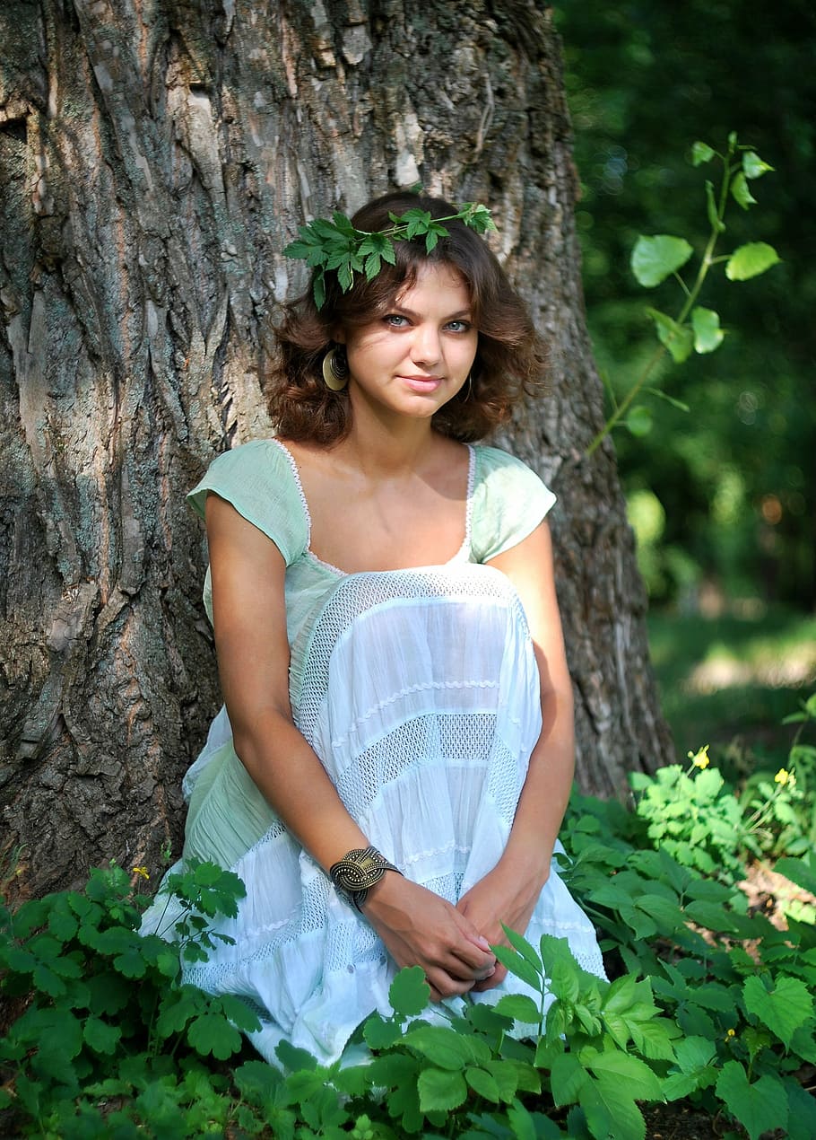 woman, wearing, teal scoop-neck cap-sleeved dress, sitting, front, tree, surrounded, green, leaf plants, nymph