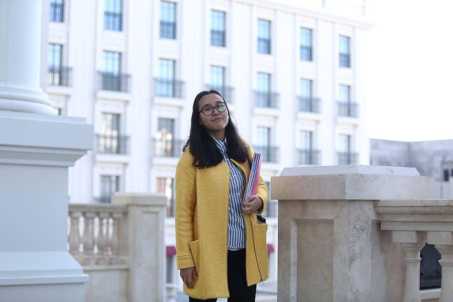 woman, wearing, yellow, cardigan, holding, pink, book, person, female, stance