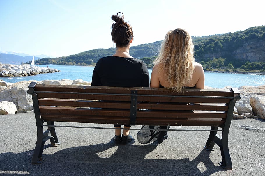 two, women, sitting, bench, body, water, mountains, daytime, sun, sea