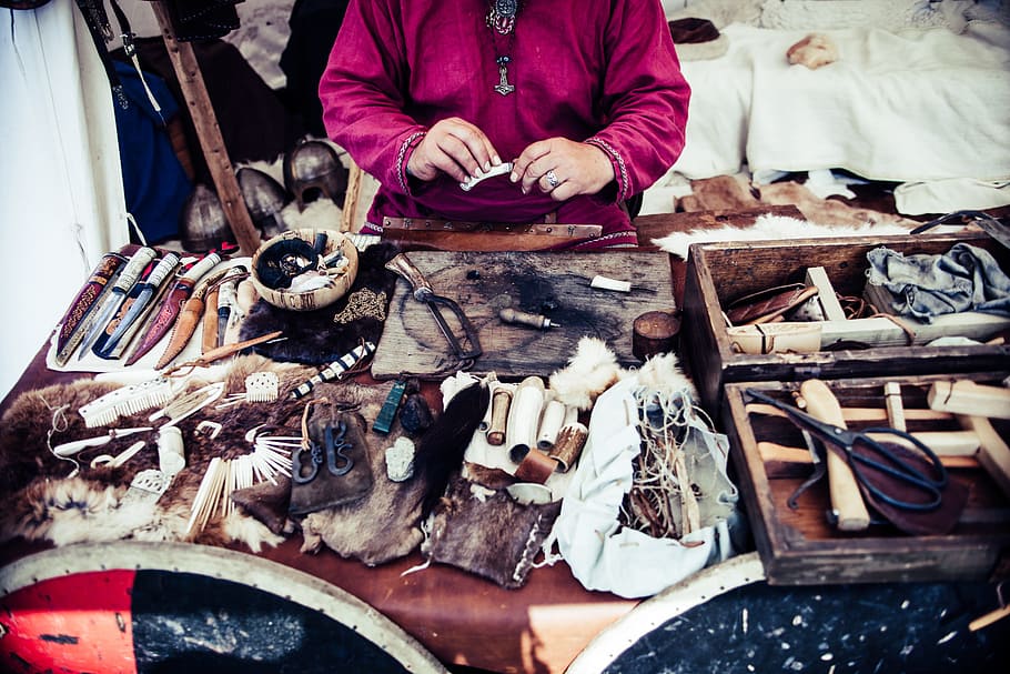 person, sitting, infront assorted-color weapon, table, crafter, crafting, craftsmanship, leather, native american, tools