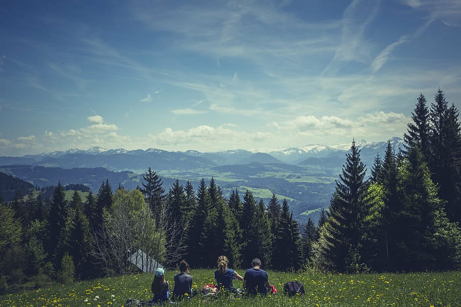 people, sitting, grass field, looking, trees, mountains, four, person, black, crew