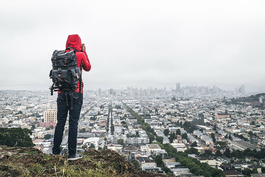 person, standing, cliff, backpack bag, back, urban, city, buildings, haze, sky