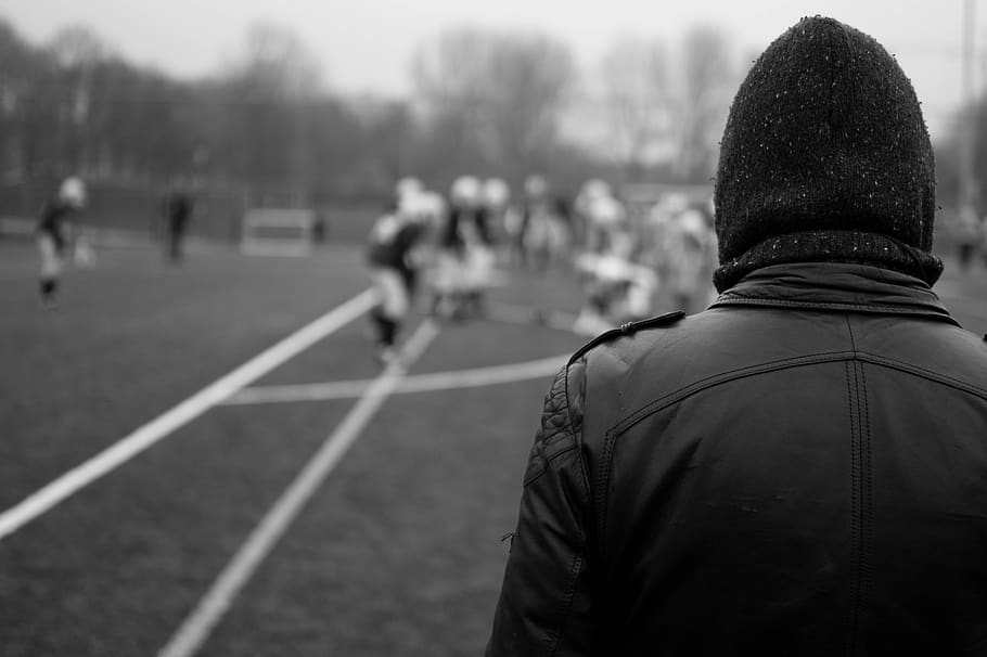 football, field, sports, athletes, spectator, leather jacket, hat, toque, beanie, rear view