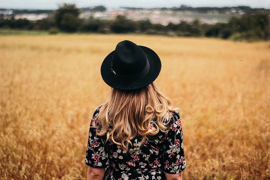woman, black, multicolored, floral, short-sleeved, top, fedora hat, standing, dried, grass field