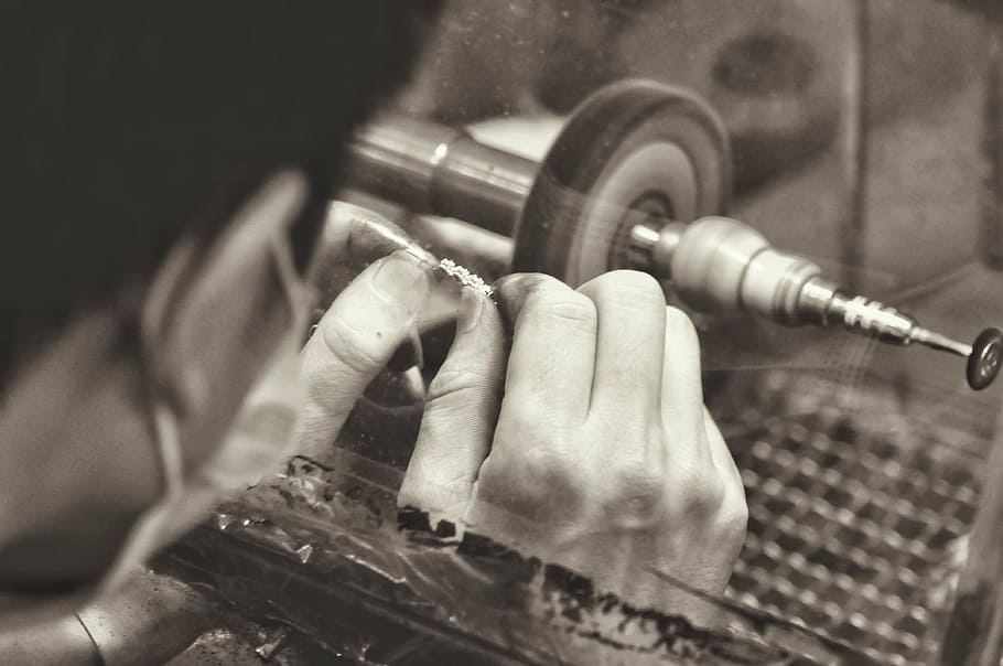 grayscale photography, man cleaning jewelry, bench grinder, jewelry manufacturing, manufacturing, polishing, work, factory, sepia, jewelry