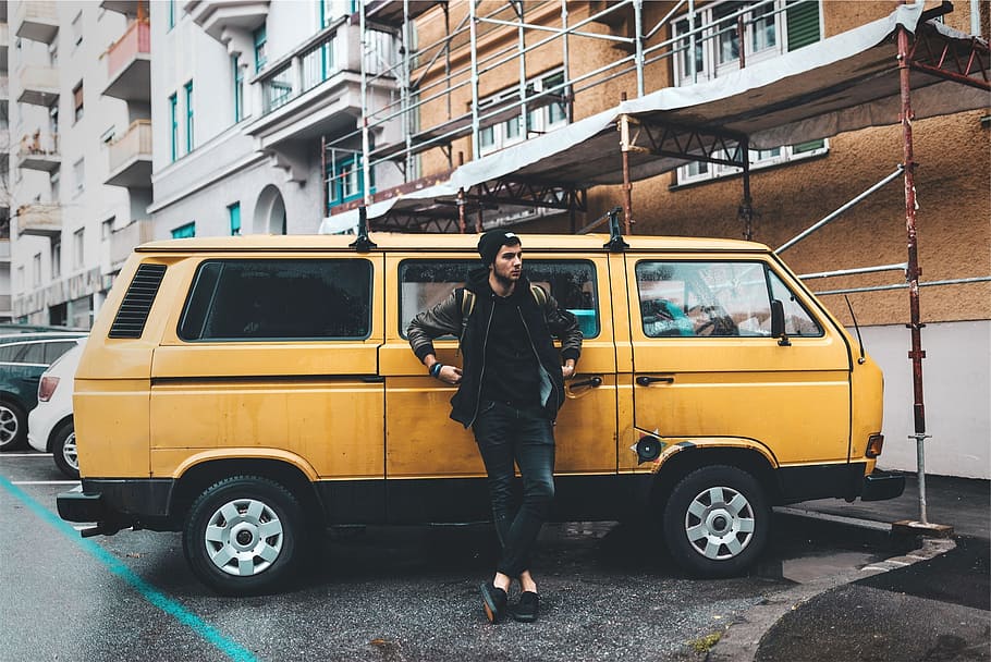 person, leaning, yellow, minivan, parked, building, van, young, guy, hat