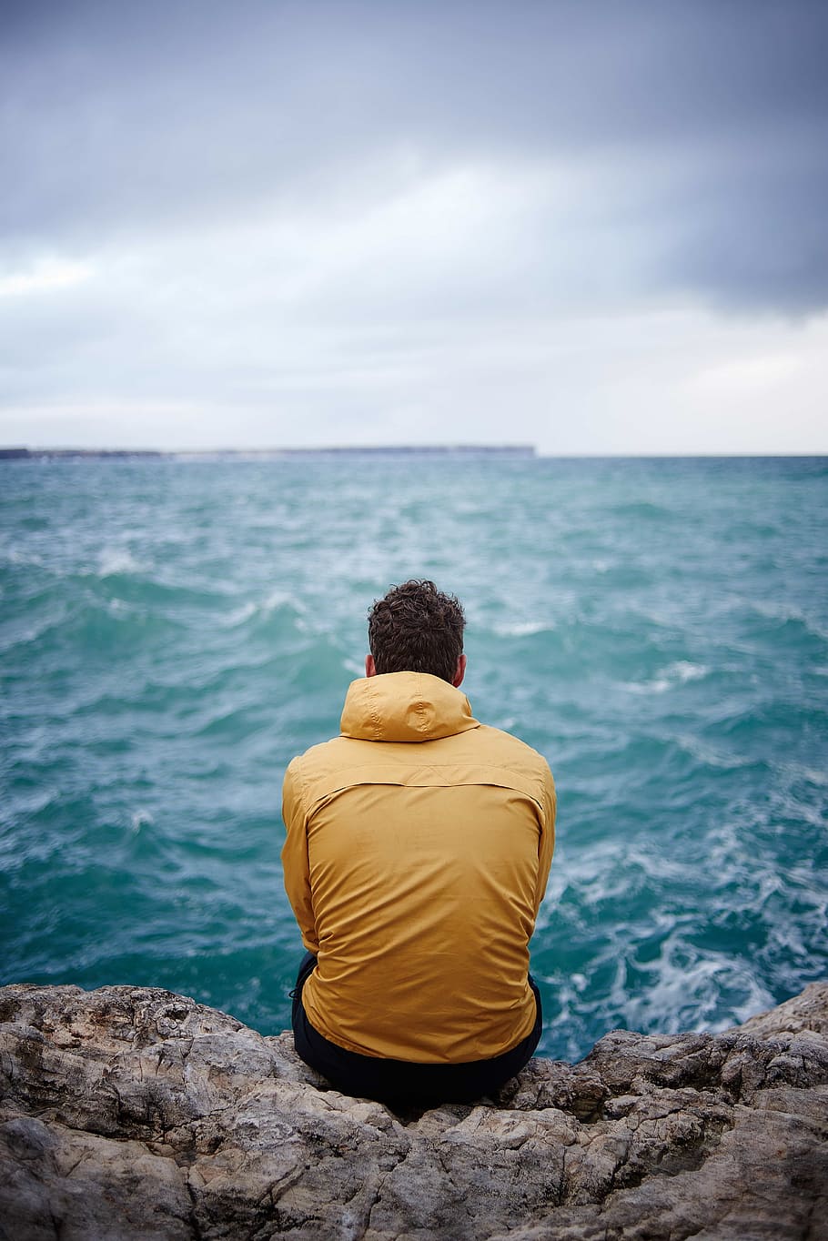 man, yellow, hooded jacket, sitting, cliff, front, sea, rough, waves, travel