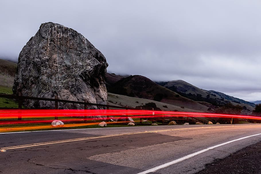 timelapse photography, vehicle, passing, road, giant rock, cloudy, sky, landscape, rocks, mountains