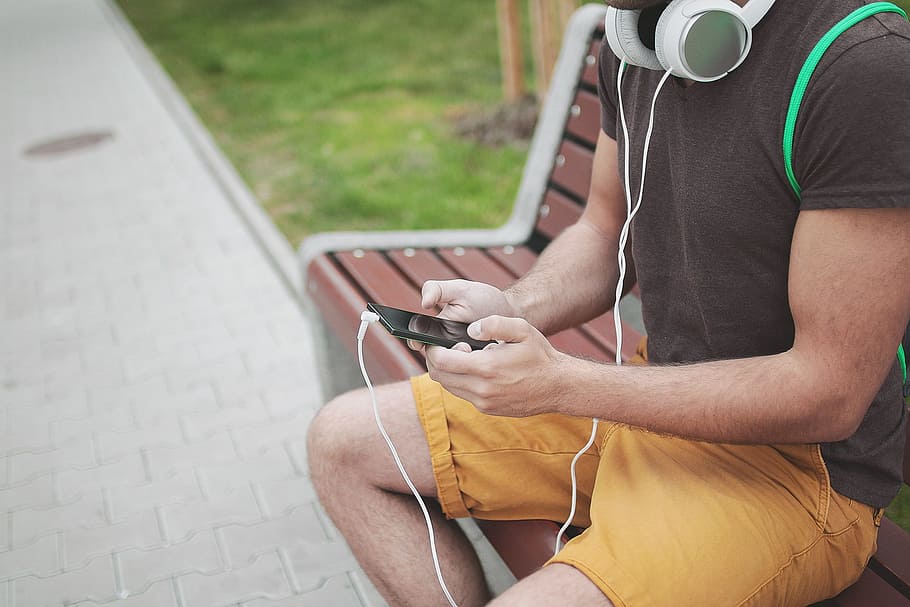 man, sitting, bench, using, smartphone, headphones, music, audio, guy, tshirt