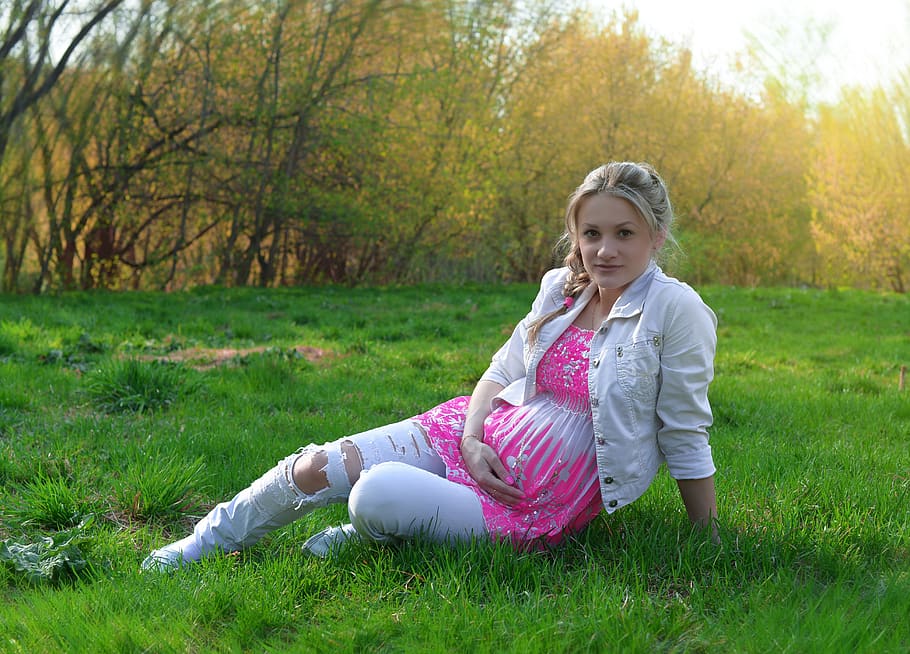 embarazo, futura madre, beremenosti, gran barriga, pronto para dar a luz, mantiene el estómago, sentada en la hierba, ropa blanca, jeans rotos, coletas