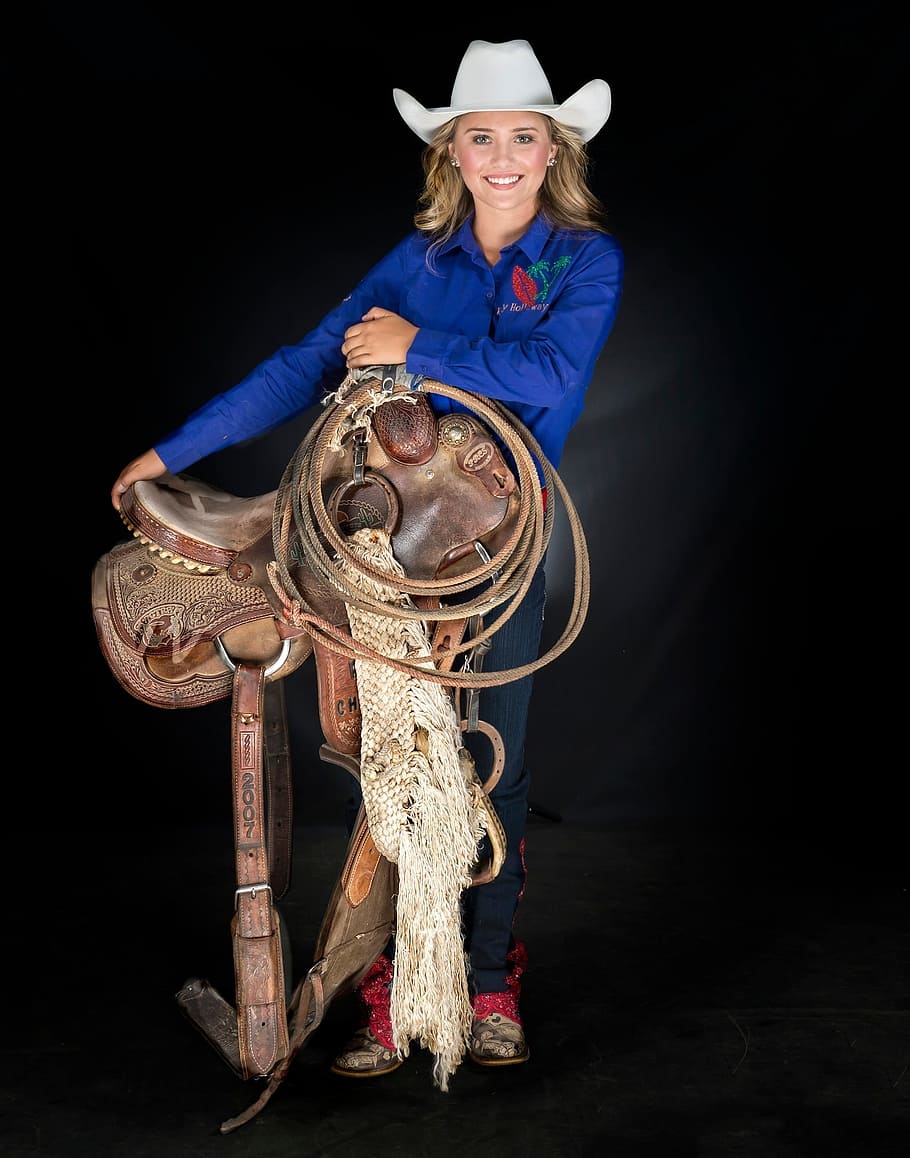 saddle, cowgirl, rider, one person, indoors, looking at camera, black background, portrait, full length, smiling