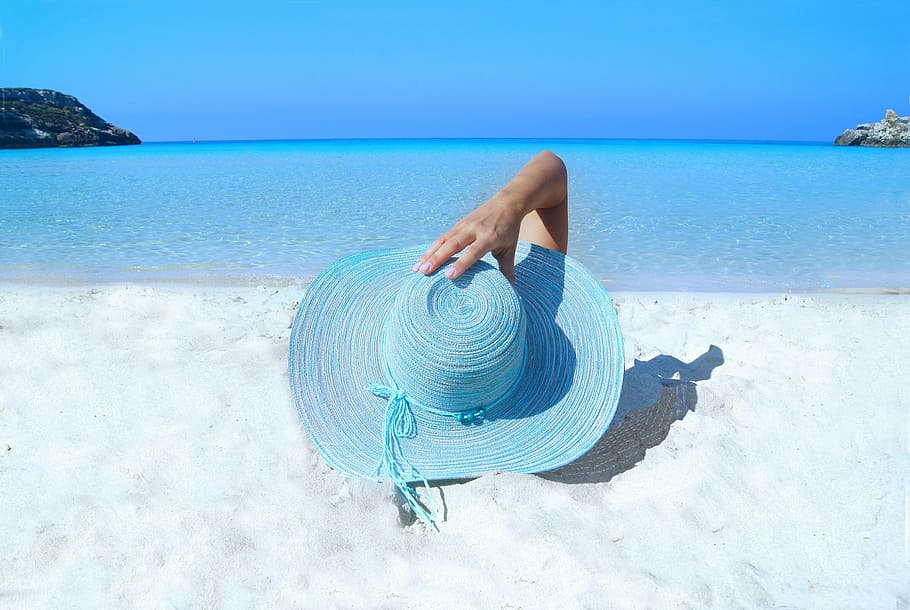 person, holding, blue, wicker sun hat, laying, white, sand, daytime, fashion, model