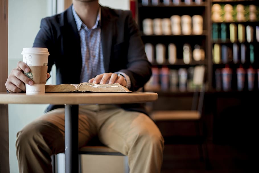 man, wearing, black, blazer, sitting, table, holding, plastic cup, book, caffeine
