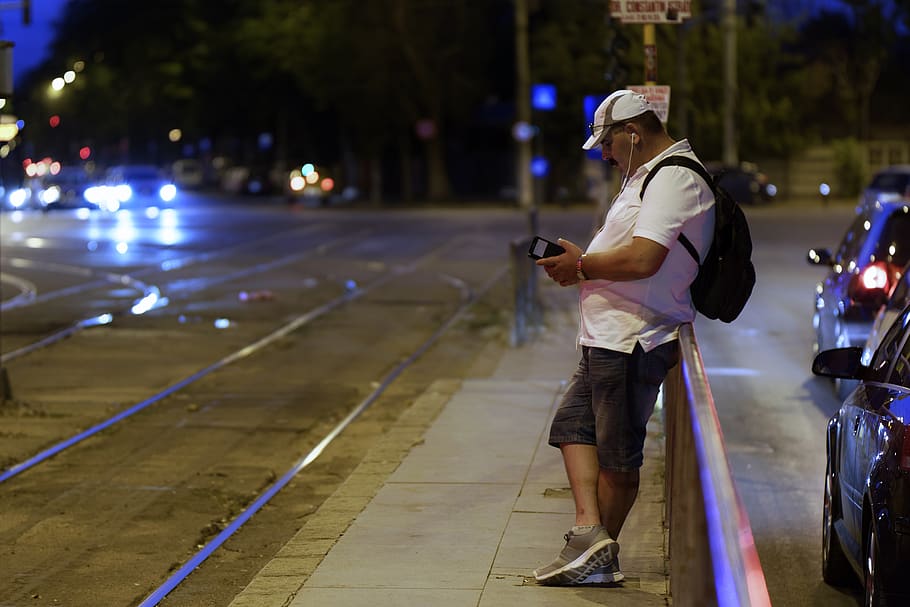 evening, the tram stop, man, backpack, cap, t-shirt, phone, waiting for, the lines for the tram, intersection