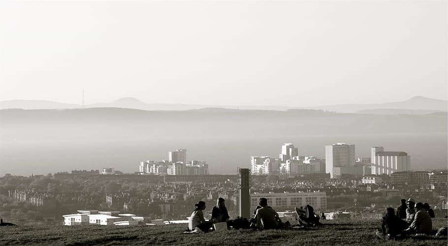fotografi grayscale, orang-orang, duduk, tanah, mencari, kota, bukit, melihat, scape, rumput