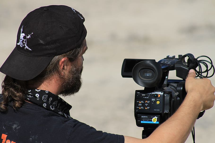 man, wears, black, cap, holding, camera, daytime, people, adult, film director