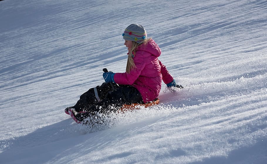 woman, wearing, pink, zip-up hooded bubble jacket, sits, orange, sled, top, snow, child