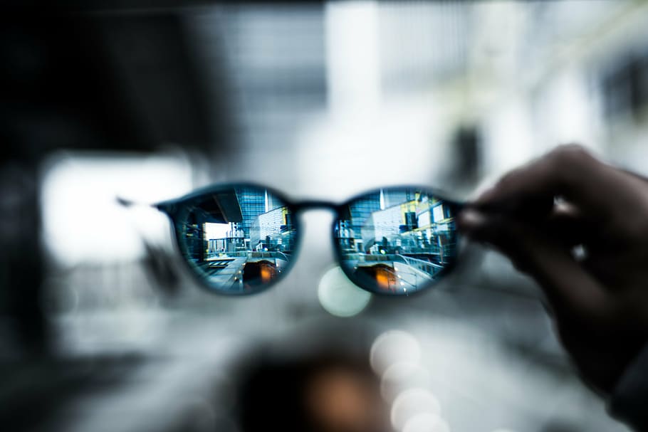 selective, focus photography, person, holding, clubmaster-style sunglasses, eyeglass, hand, bokeh, blur, building