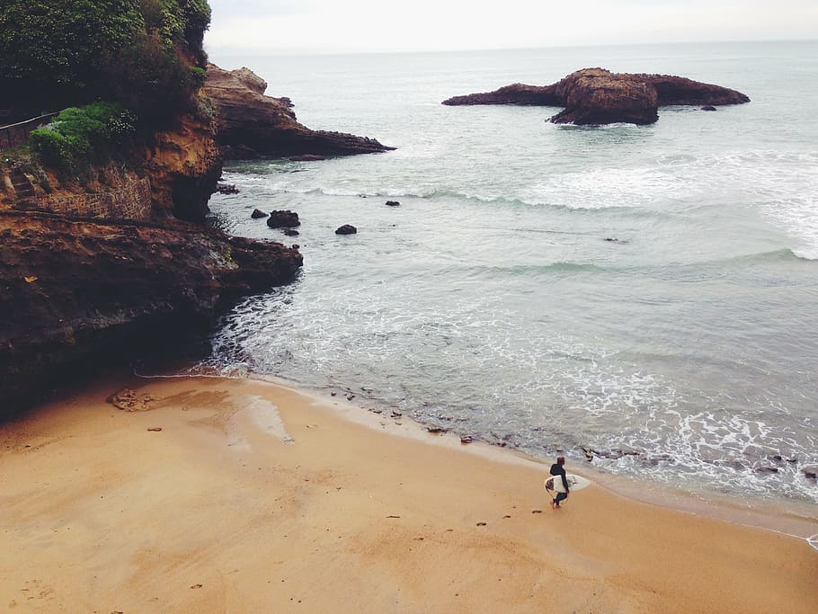 person, holding, surfboard, walking, seashore, black, shirt, daytime, beach, sand