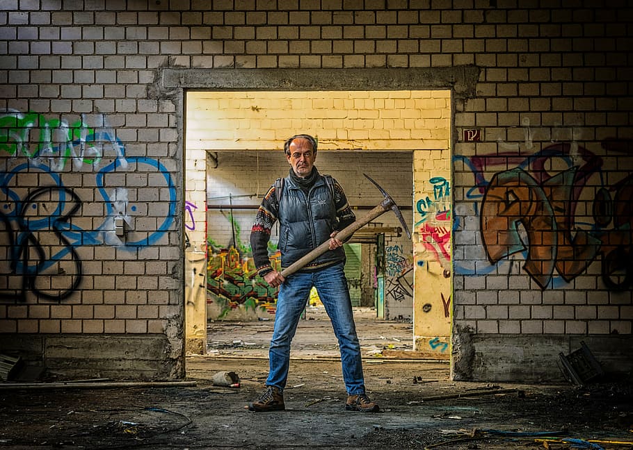 man, wearing, black, vest, blue, jeans, holding, pickaxe, behind, wall