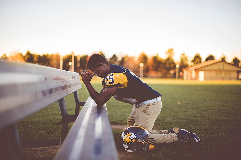 football player, praying, bench, man, people, kneel, helmet, playground, field, blur