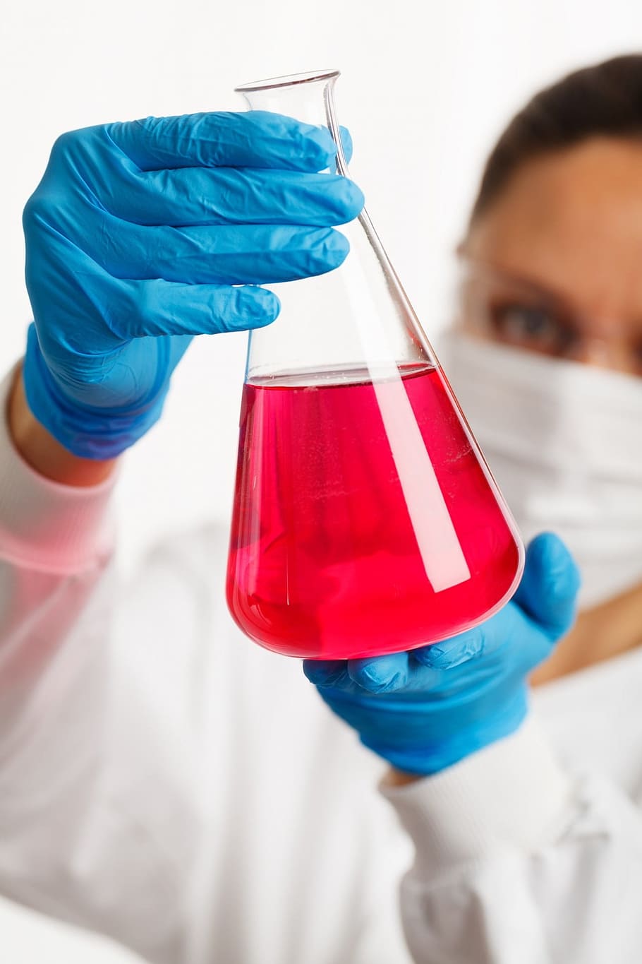 person, white, laboratory gown, blue, gloves, holding, clear, glass laboratory flask, red, liquid