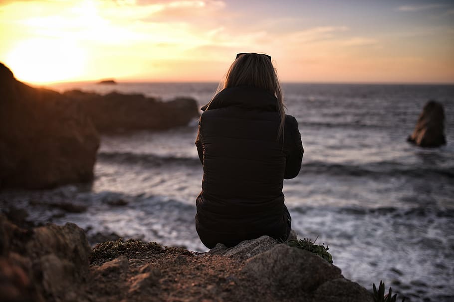 Mujer, sentado, roca, vistiendo, negro, chaqueta, cerca, océano, niña, puesta de sol