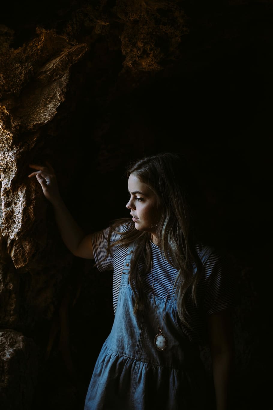 woman, blue, chambray, overall, skirt, holding, rock surface, woman in blue, rock, surface