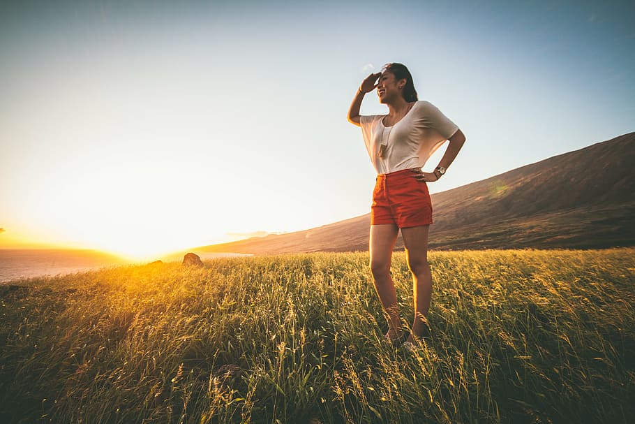 woman, standing, green, grass field, orange, shorts, stands, field, sunset, mountain