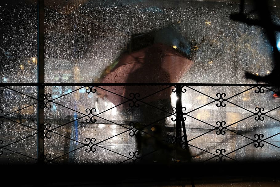black steel fence, dark, people, silhouette, outside, rain, raining, umbrella, night, one person