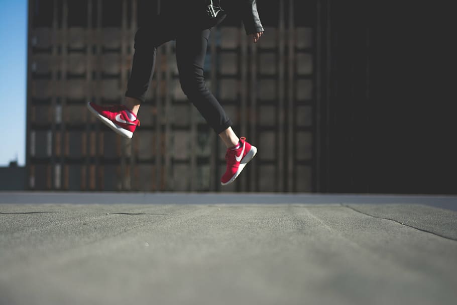person, wearing, red, nike sneakers, jumping, road, day, black, jeans, nike