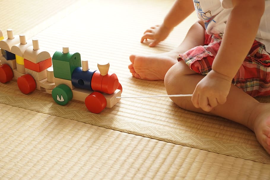 baby, wearing, white, shirt, holding, assorted-color, wooden, train toy, sitting, brown