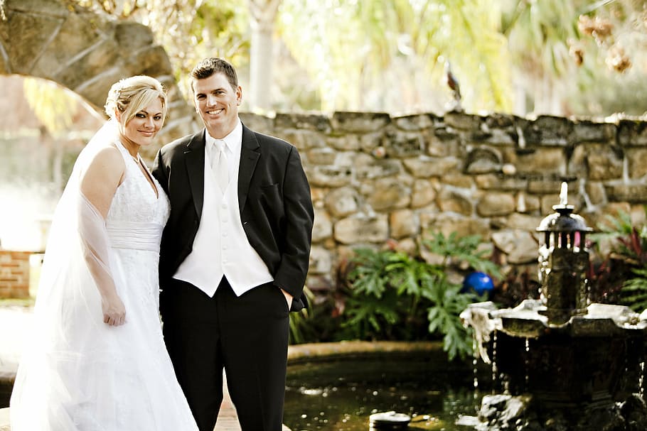 man, black, suit, woman, white, wedding dress, standing, garden fountain, daytime, bride
