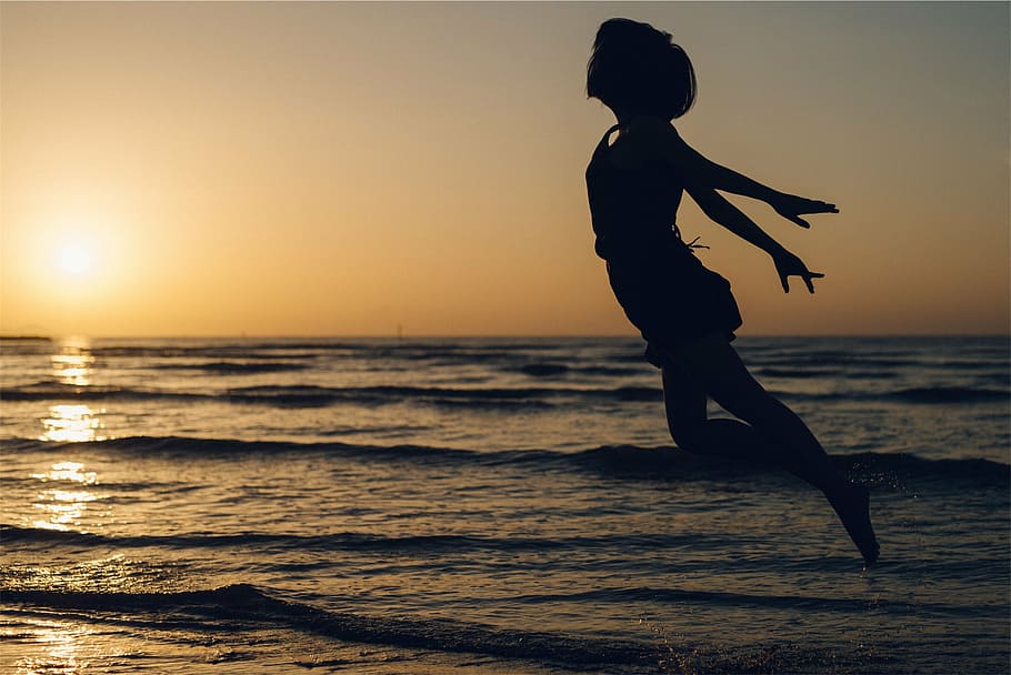 mujer, saltando, mediados, aire, orilla del mar, silueta, durante el día, puesta de sol, anochecer, volando