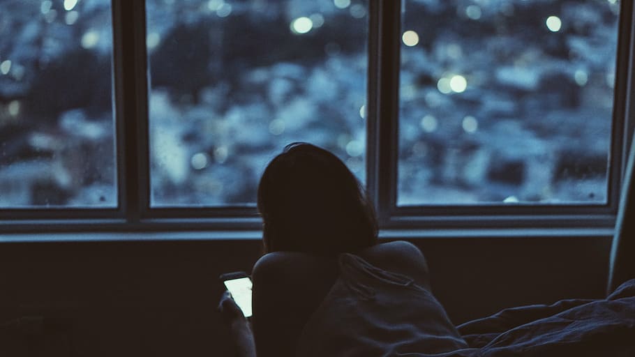 woman, holding, smartphone, lying, bed, boke lights background, person, near, window, people
