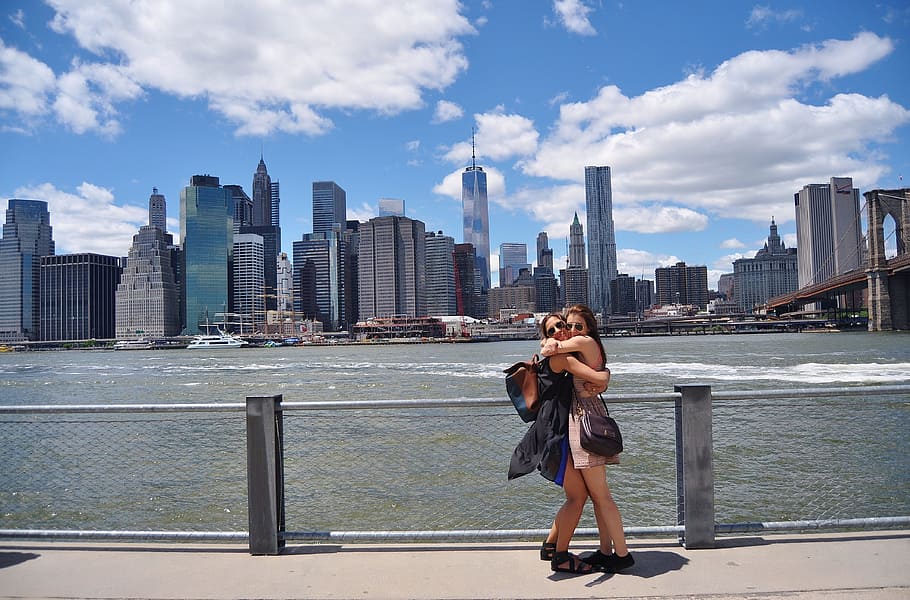two, women, hugging, wire fence, gray, clouds, building, faraway, new, york