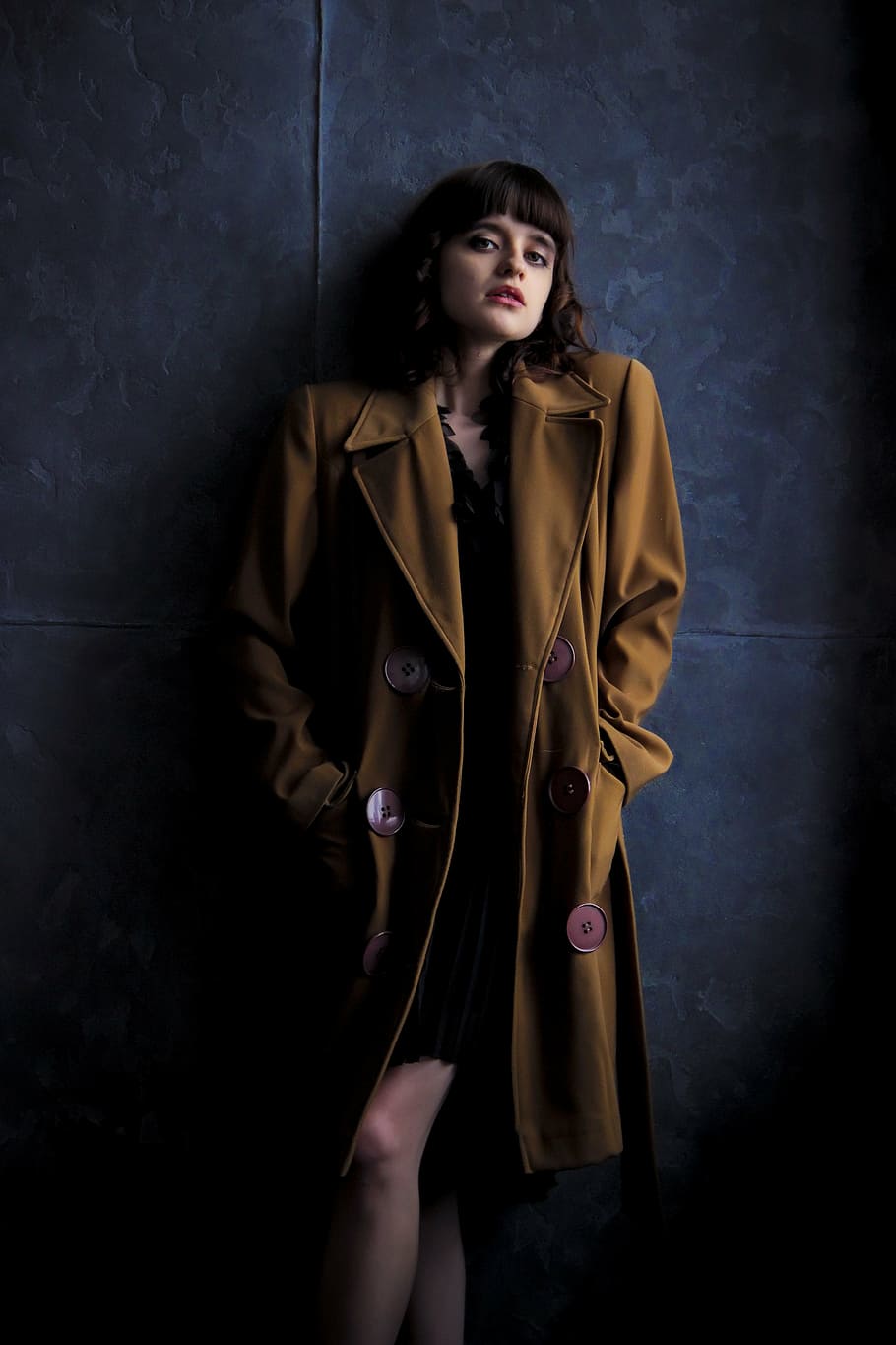 woman, wearing, brown, trench coat, stands, next, blue, painted, wall, girl