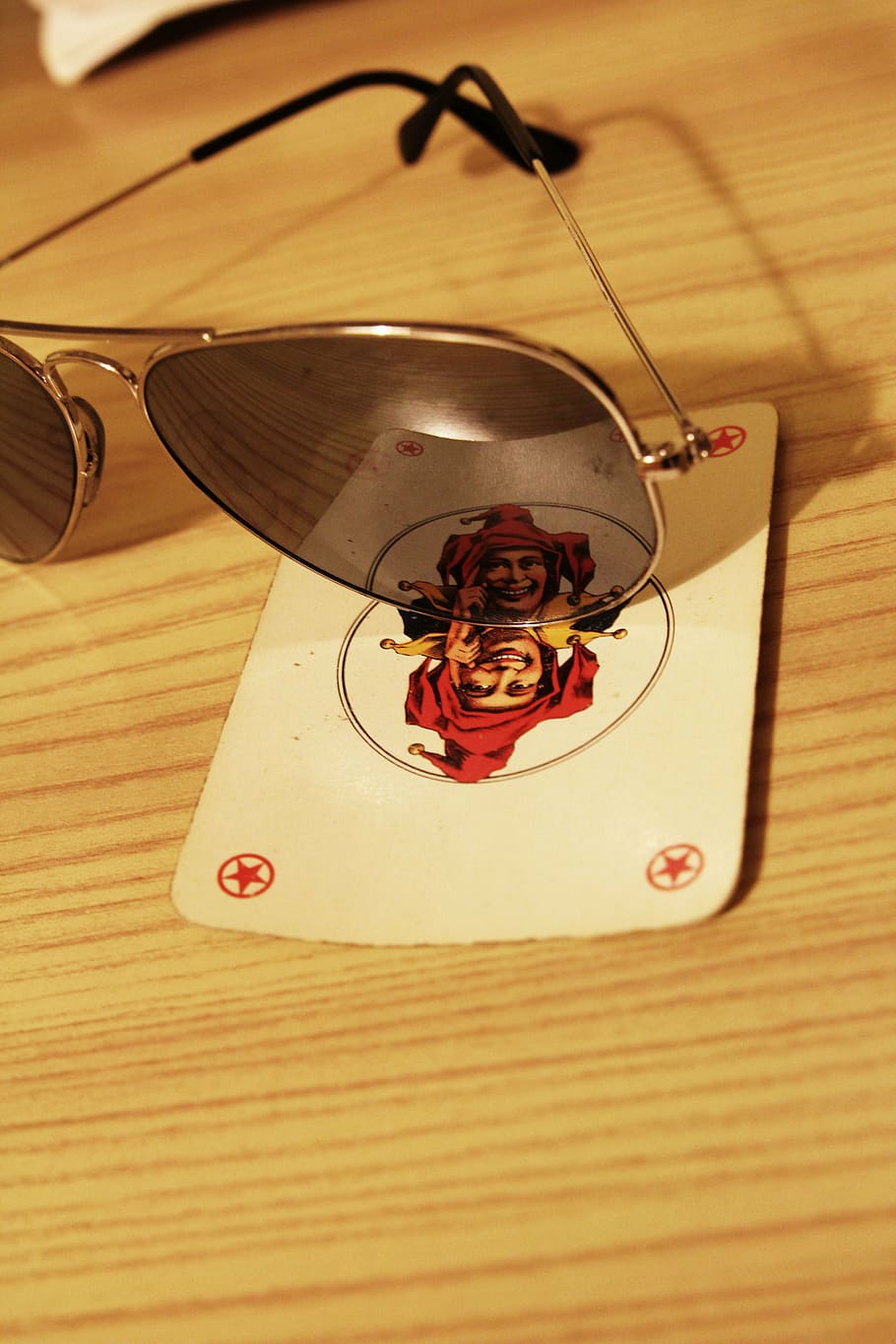 sunglasses, playing card, wildcard, joker, wood, table, mirror, red, close-up, indoors