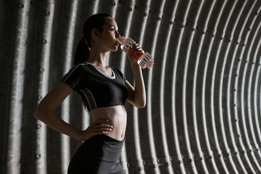 young athletic woman, drinking a tonic drink, transparent plastic bottle, gray gloomy tunnel, close-up, one person, standing, lifestyles, young adult, holding