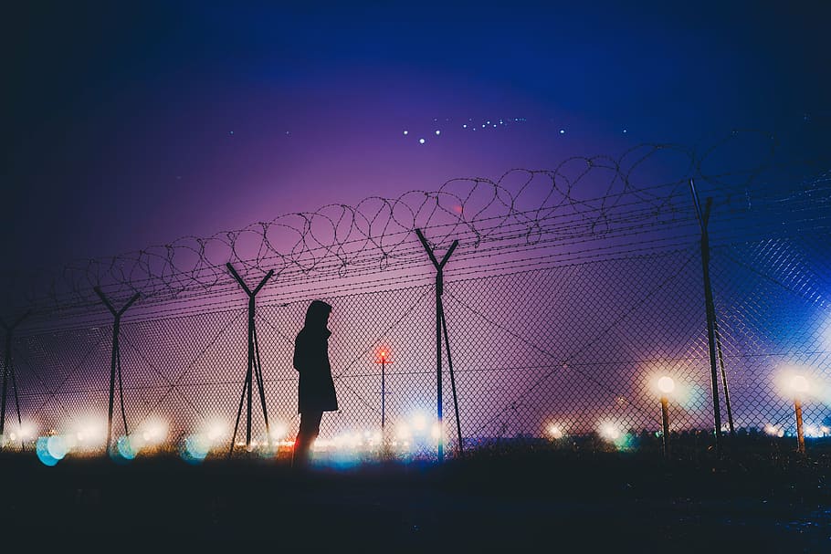 silhouette photograph, person, standing, link fence, woman, fence, dark, night, sky, lights