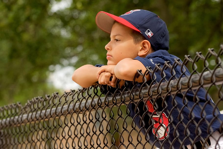 boy, wearing, blue, mlb cap, leaning, gray, fence, baseball, cleveland, park