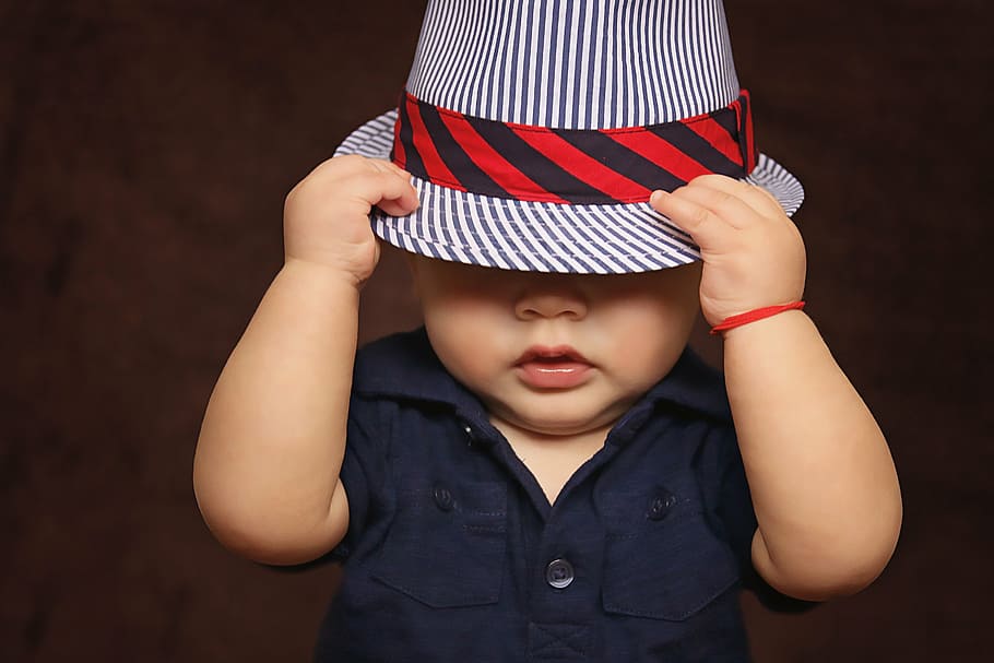 Bebé, vistiendo, azul, top, blanco y azul fedura, niño, sombrero, cubierto, ojos, jugando