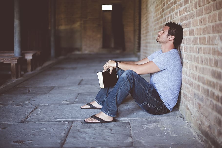 man, wearing, gray, shirt, holding, book, sitting, brick wall, alone, bricks